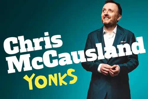 Comedian Chris McCausland wears a suit as he stands against a turquoise background.